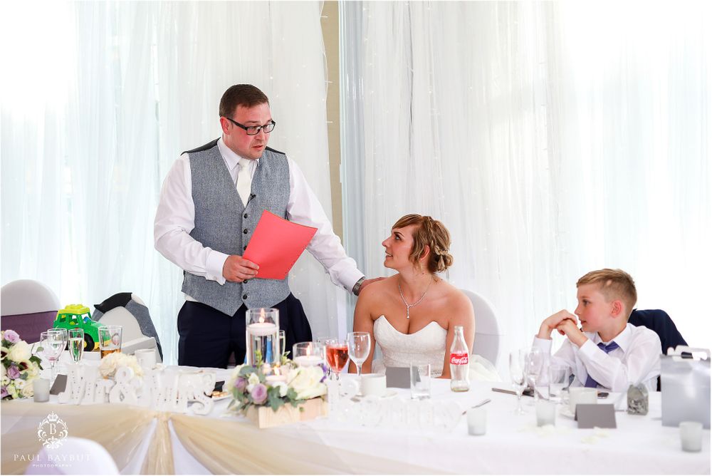 Wedding reception speech moment at elegant white-themed dining table setup.