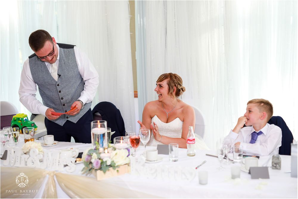 Reception table scene with guests enjoying speeches during wedding celebration.