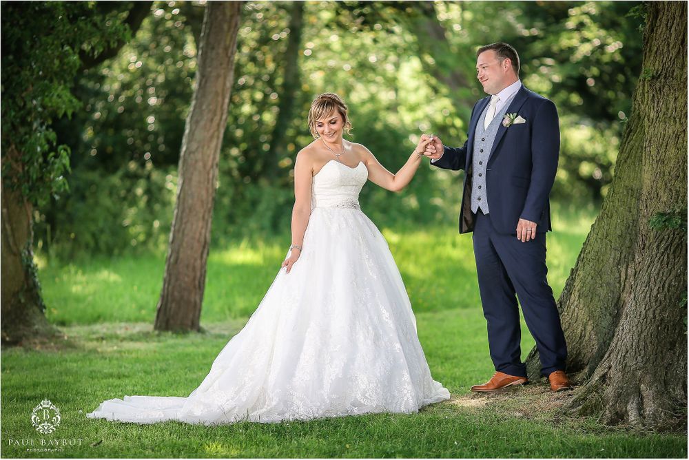 Romantic outdoor wedding portrait with couple posing between trees on a sunny day.