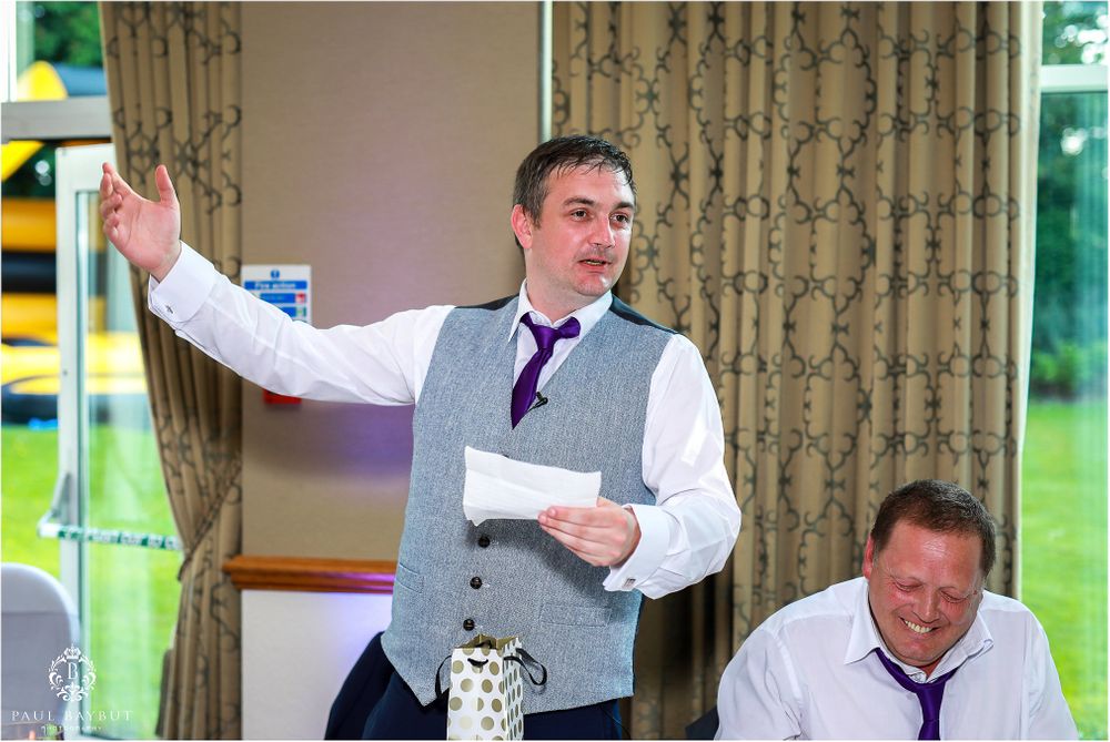 Wedding reception speaker giving toast at head table during celebration.