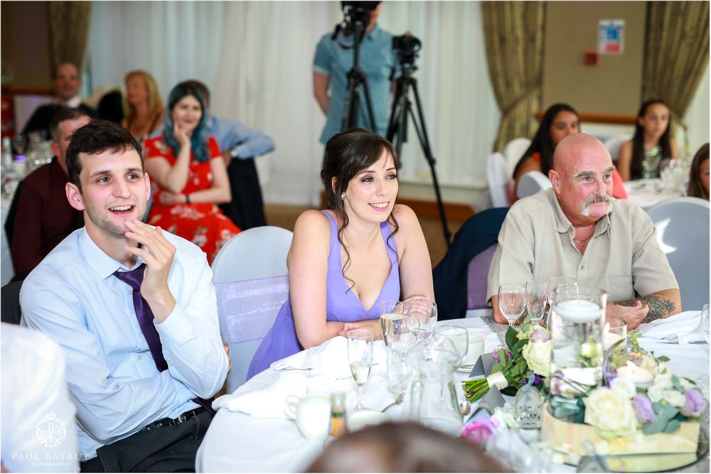 Wedding reception guests enjoying speeches and entertainment at decorated dining tables.