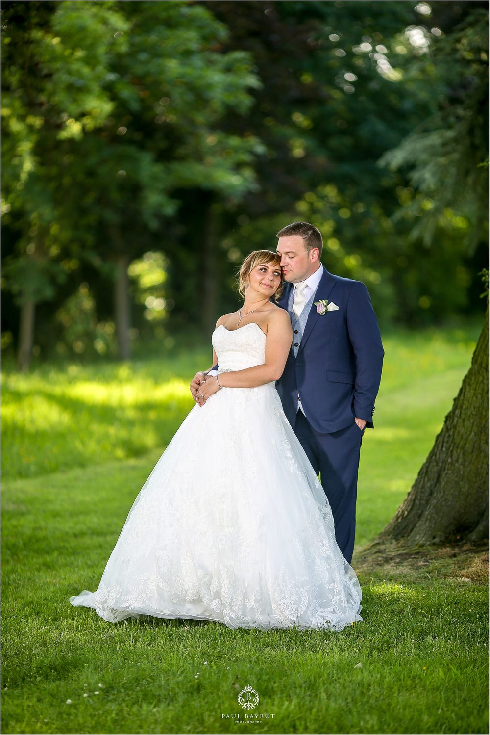 Elegant wedding portrait in a sunlit garden with white ball gown and navy suit.