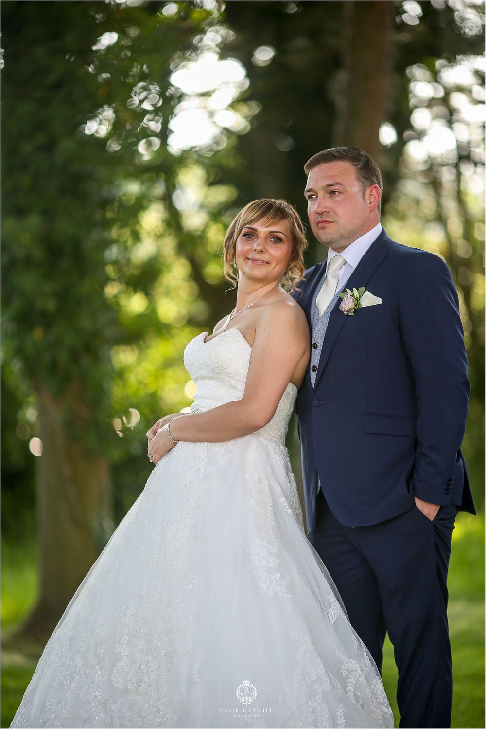 A wedding couple poses outdoors in a romantic forest setting with soft bokeh lighting effects.