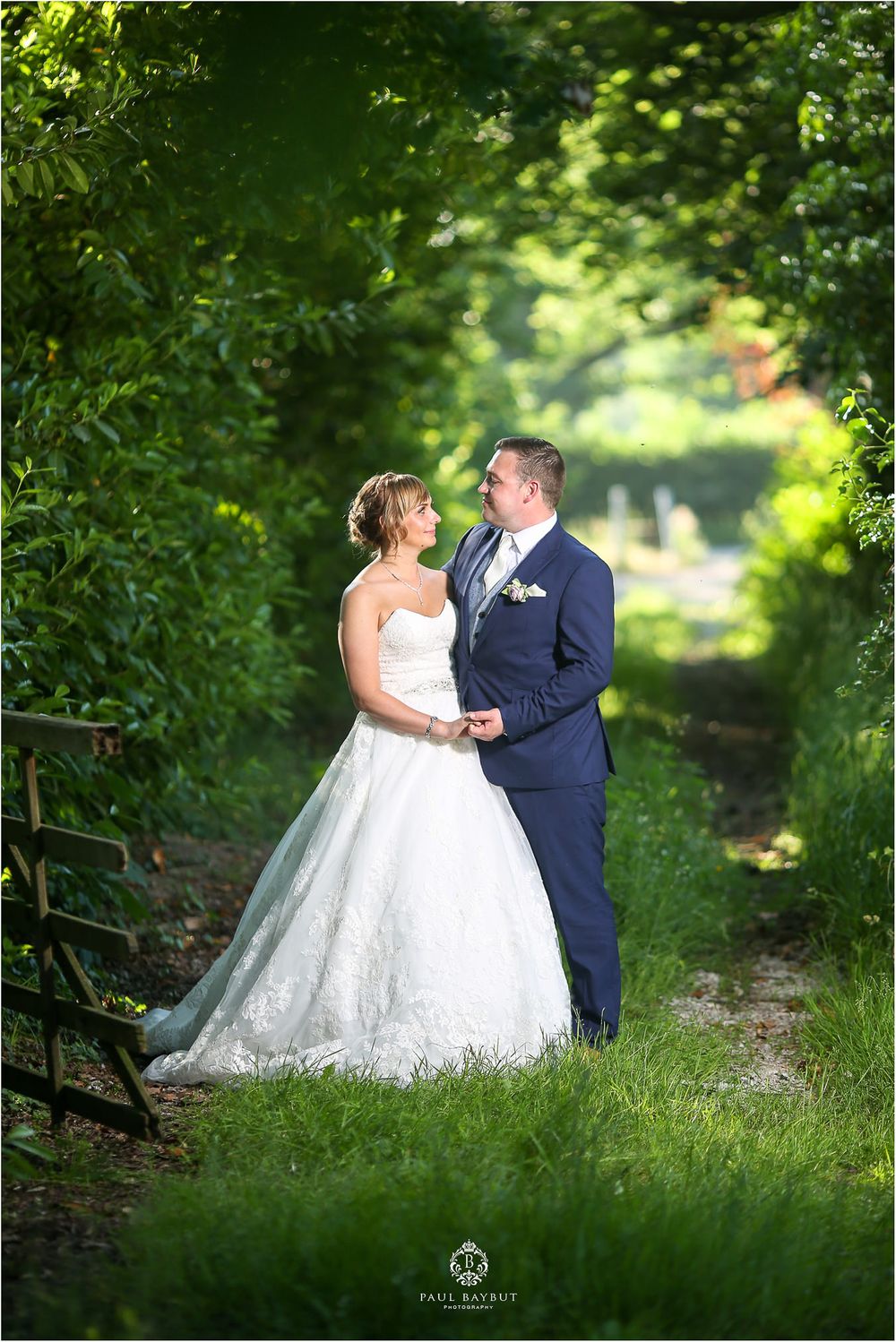 A romantic wedding photo on a tree-lined path with a couple embracing in formal attire.