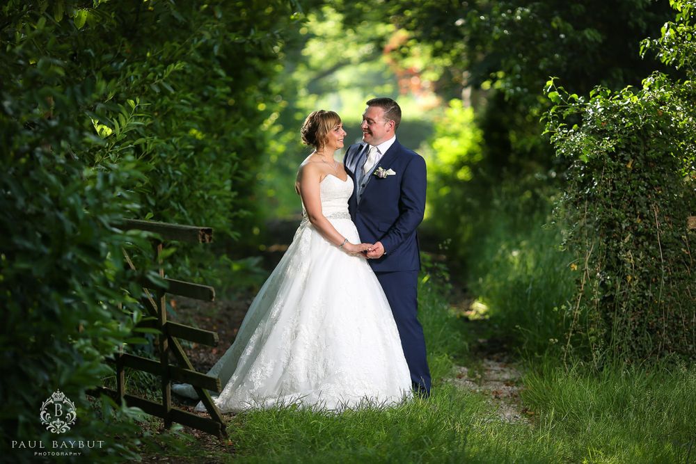 A scenic wedding portrait set on a garden path with a wooden bench in the background.