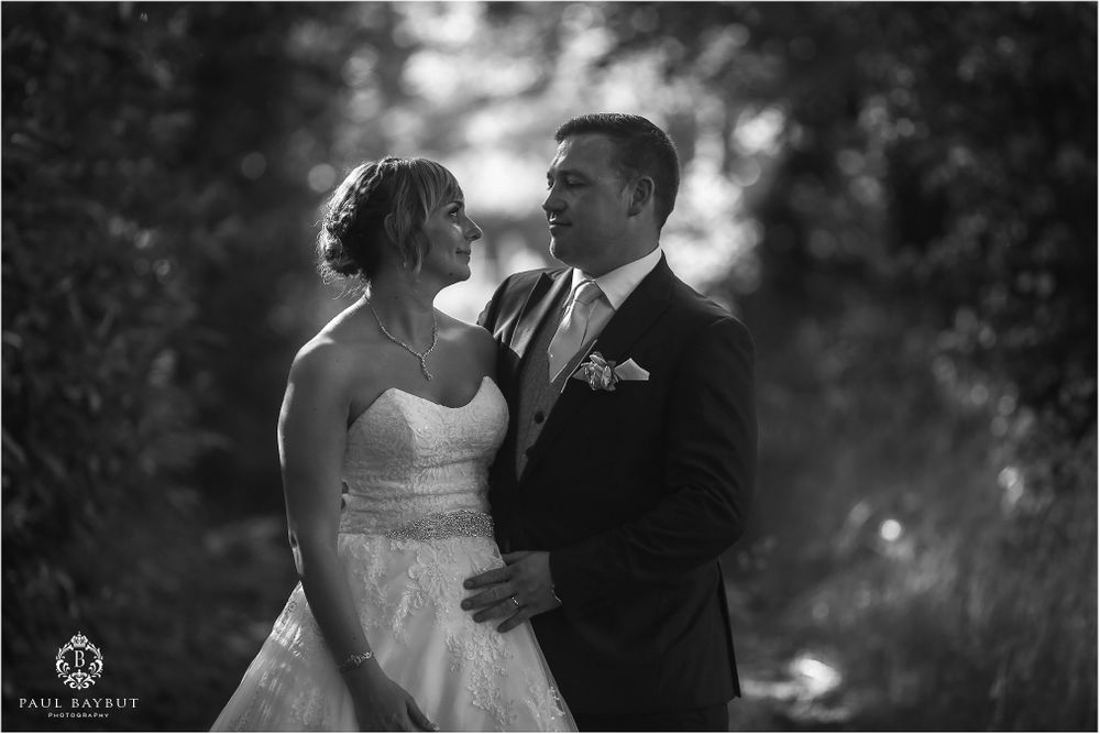 A black and white wedding portrait capturing an intimate moment in a garden setting.