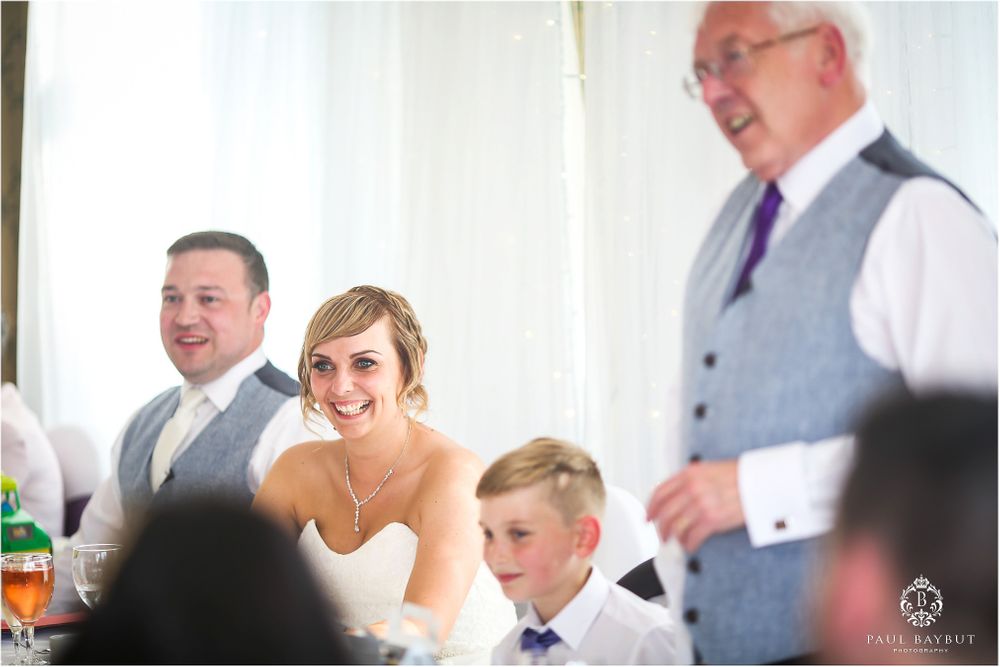Wedding reception guests listening to speeches in a bright indoor venue.