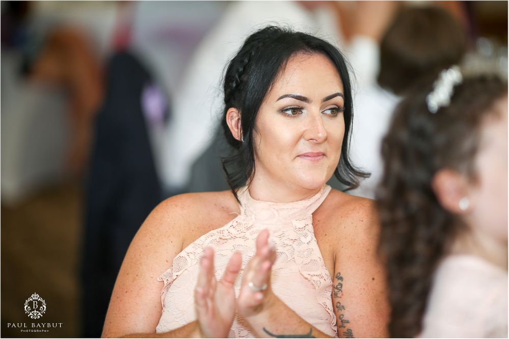 Wedding guest in pink lace dress applauding during reception celebration.