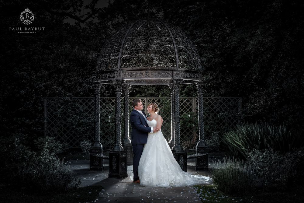 A romantic nighttime portrait of newlyweds standing in an ornate garden gazebo.
