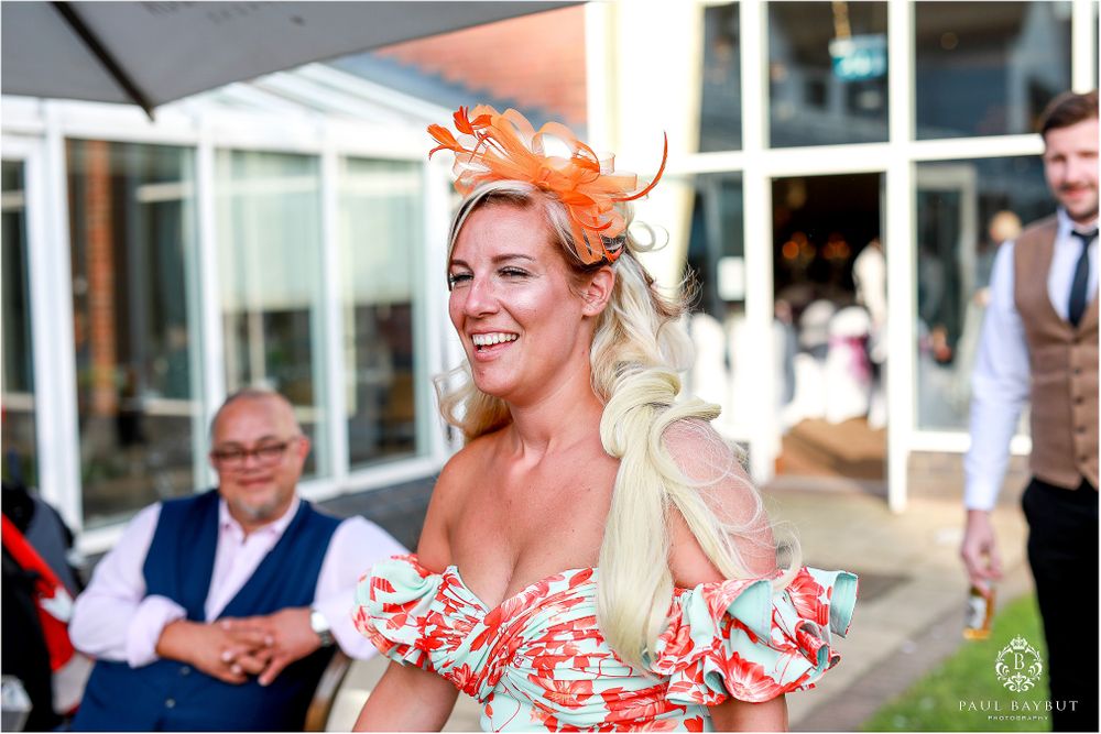 A vibrant wedding celebration scene with an orange fascinator and festive atmosphere.