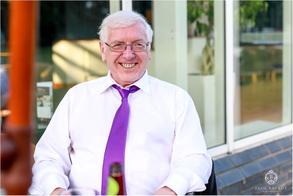 A cheerful guest wearing a white shirt and purple tie at an outdoor wedding reception.