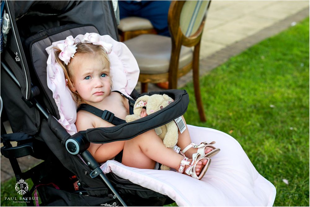 Baby sits comfortably in a stroller on grass during an outdoor event.
