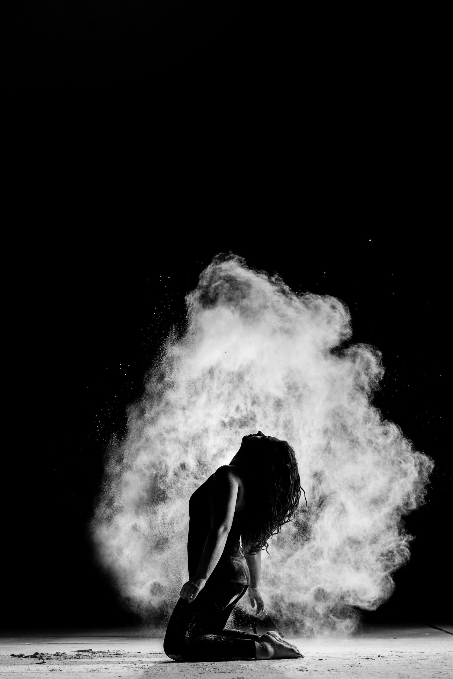 A dramatic black and white silhouette of a kneeling figure surrounded by an ethereal cloud of white powder or smoke.