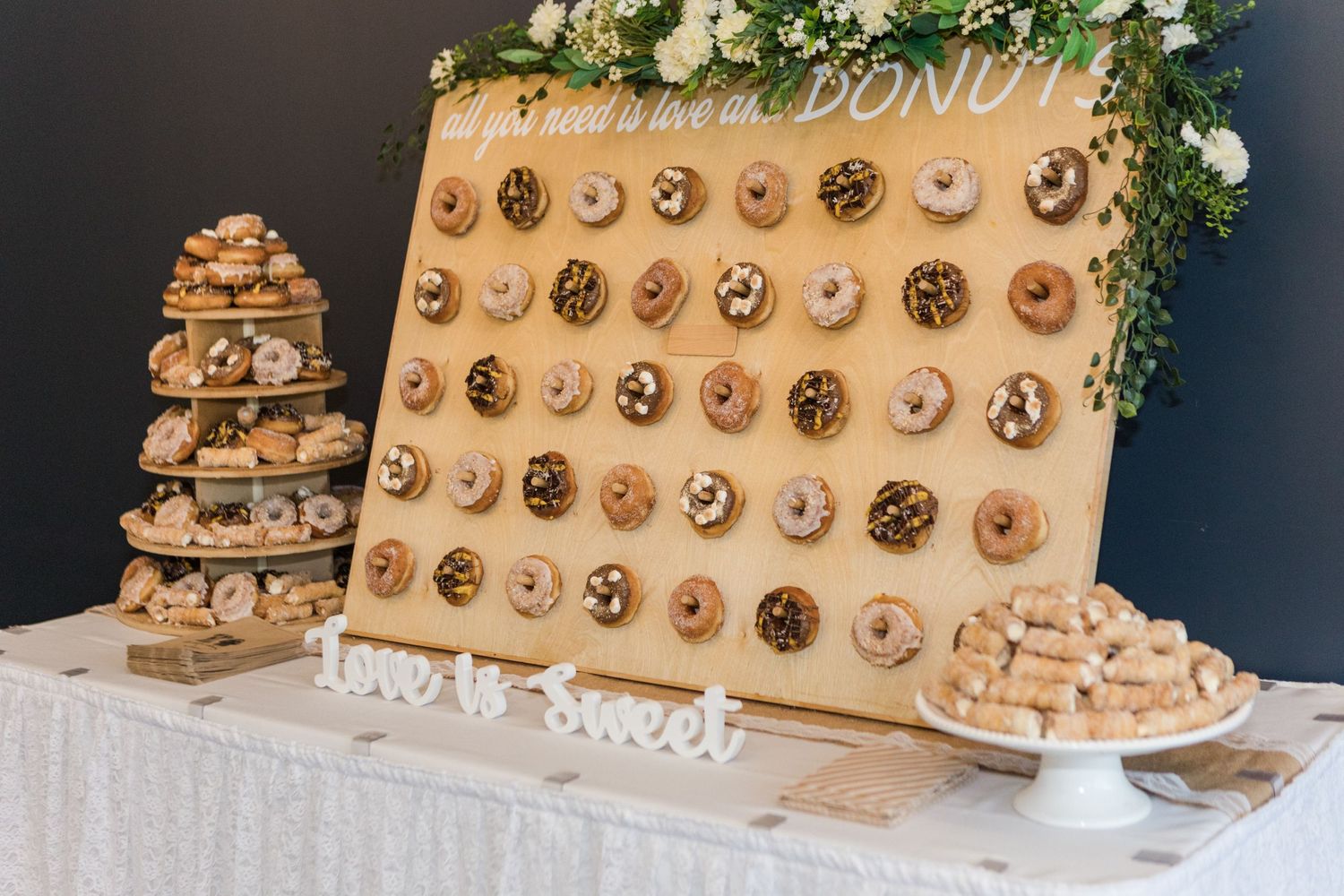 Rustic wooden donut wall display with assorted donuts at wedding reception.