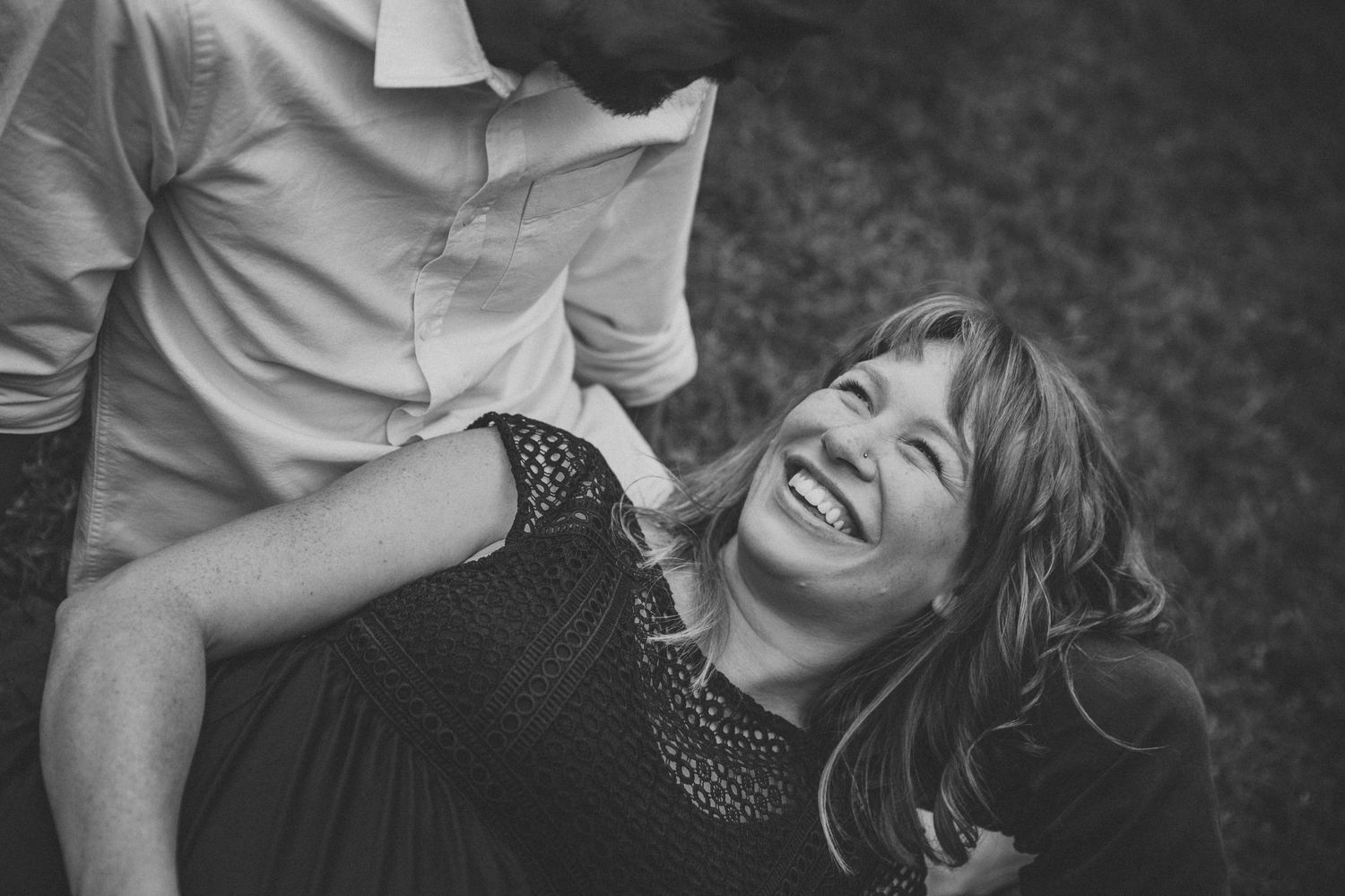 A joyful candid black and white portrait of someone lying on grass and laughing.