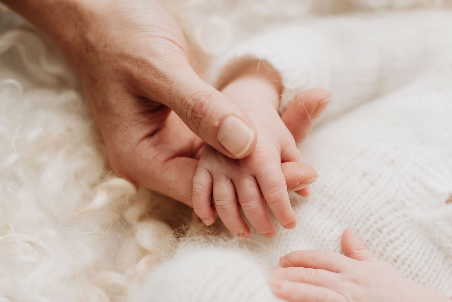 Close-up of adult and baby hands touching gently on white fabric.