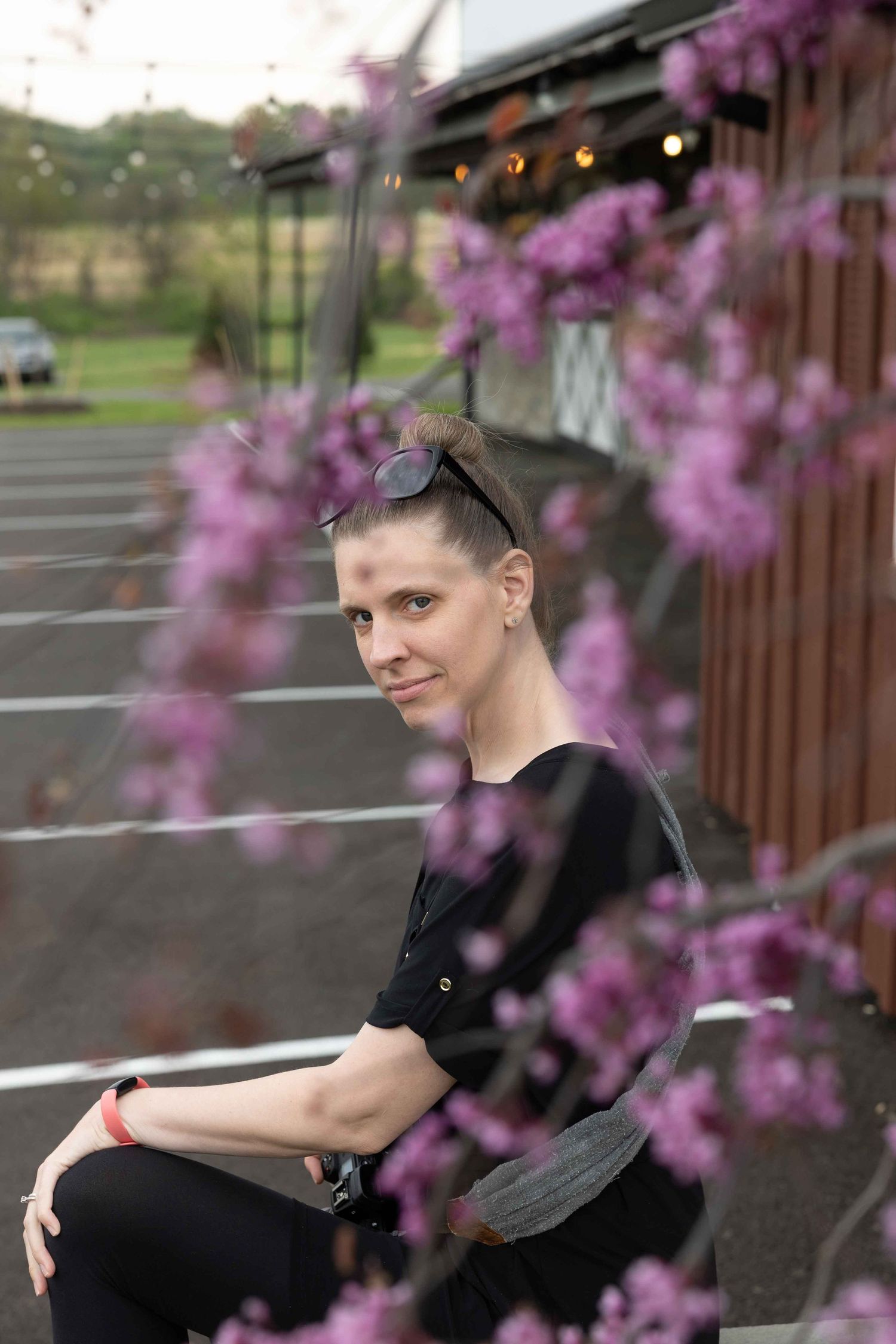 A figure seated outdoors with blooming pink flowers in the foreground.