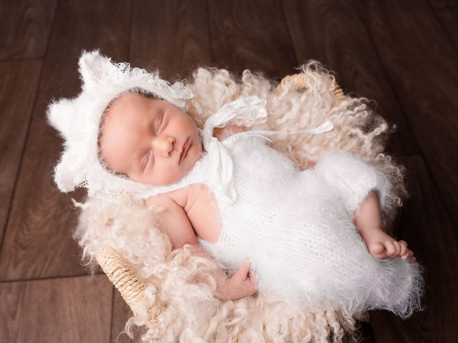 Newborn baby girl wearing white fluffy outfit and lace hat, in a rattan basket, at newborn photoshoot in Doncaster.