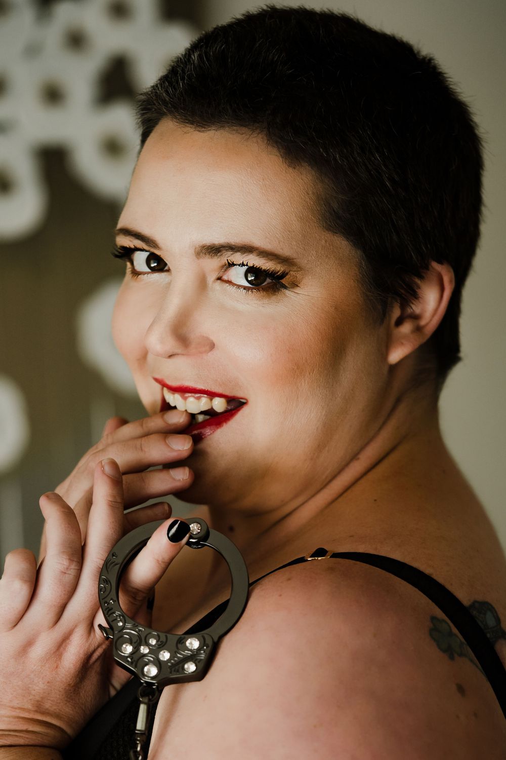 short haired woman in red lipstick holding bling handcuffs and smiling in boudoir