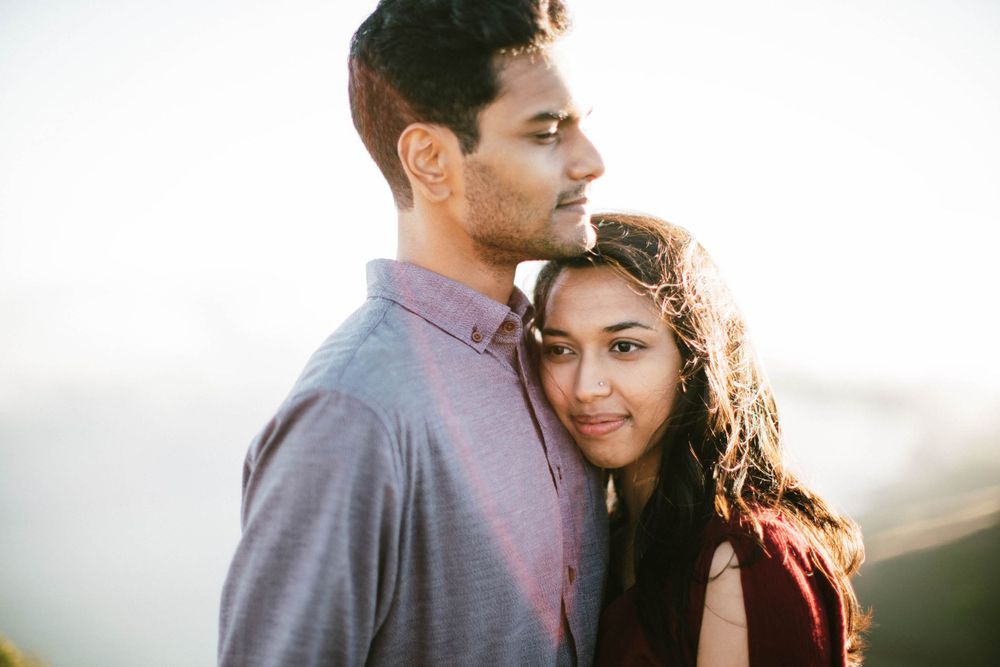 Romantic couple sharing tender moment with sunlit coastal mountains in background.