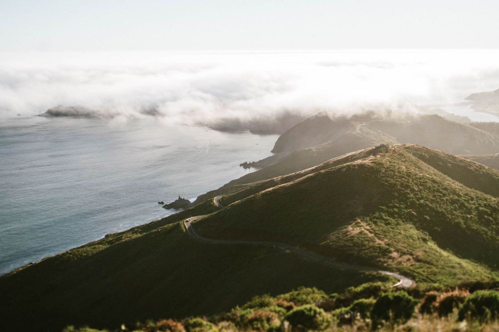 Dramatic coastal landscape with winding ridge trail and low-lying fog over ocean.