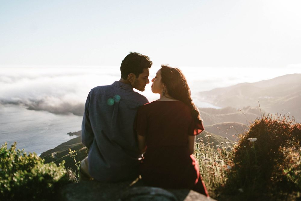 Intimate moment shared between couple on mountaintop with misty ocean backdrop.