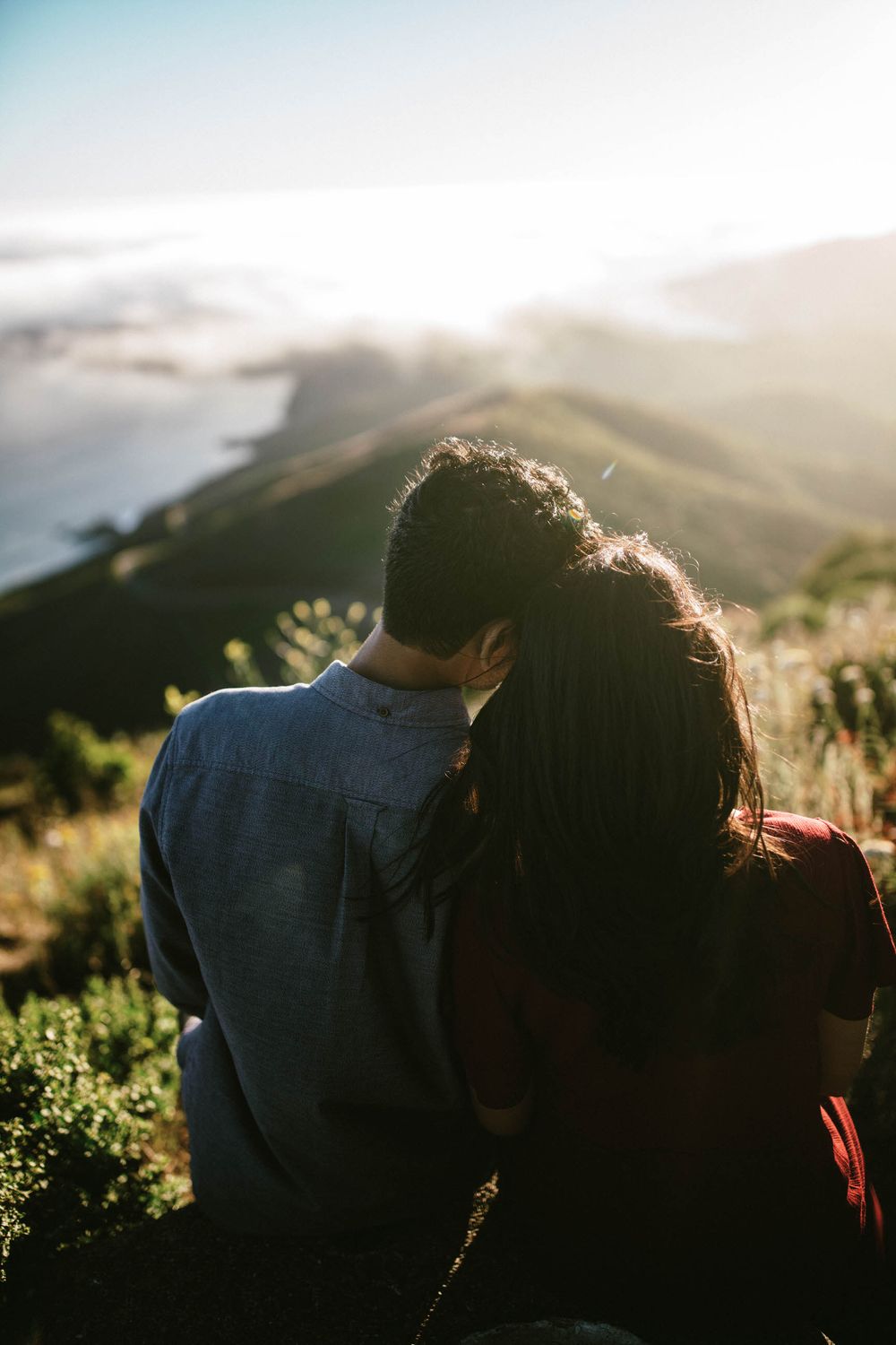 Silhouetted couple enjoying sunset views from mountain peak above foggy coastline.