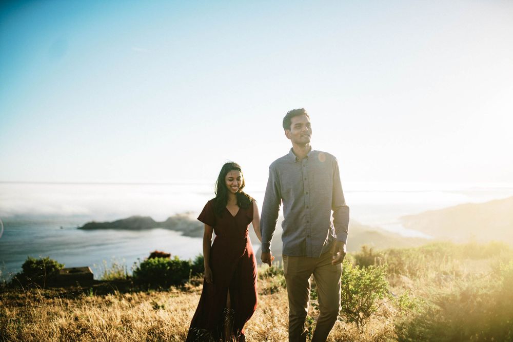 Two people walking along mountain ridge with misty ocean views at golden hour.