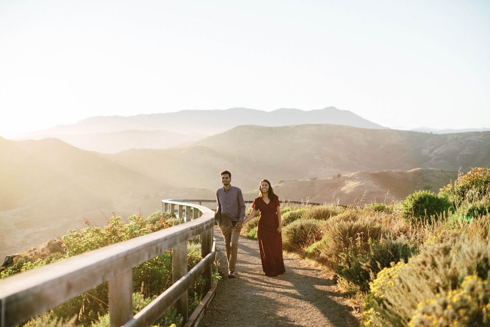 A couple walks along a scenic mountain path during golden hour sunset.