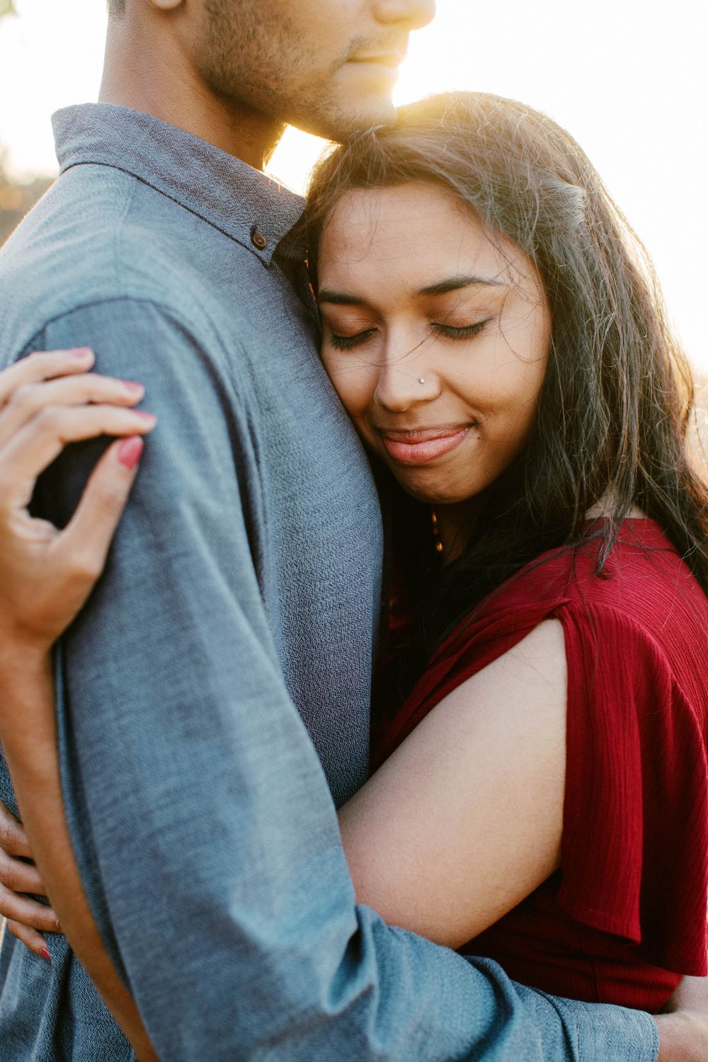 A tender embrace between a couple wearing red and blue during sunset.