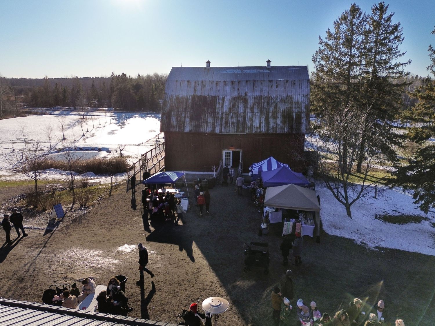 Large rustic barn building with outdoor vendor tents and gathering space in snowy setting.