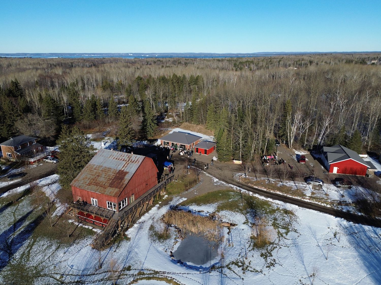 Birds eye view of rural property showing rustic red barn and surrounding buildings in winter landscape.
