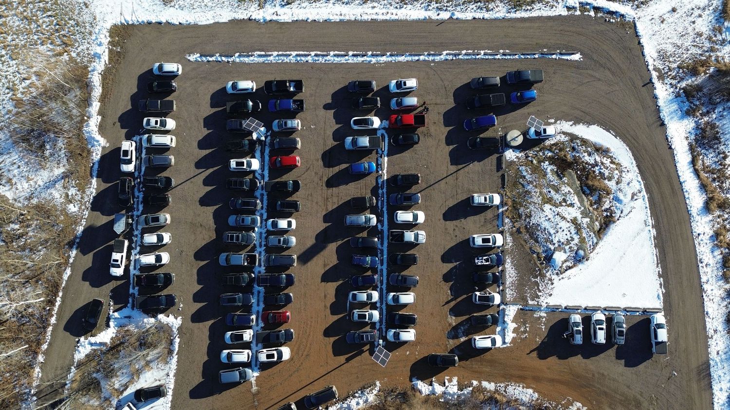 Overhead drone shot of organized parking lot with rows of cars on snowy ground.