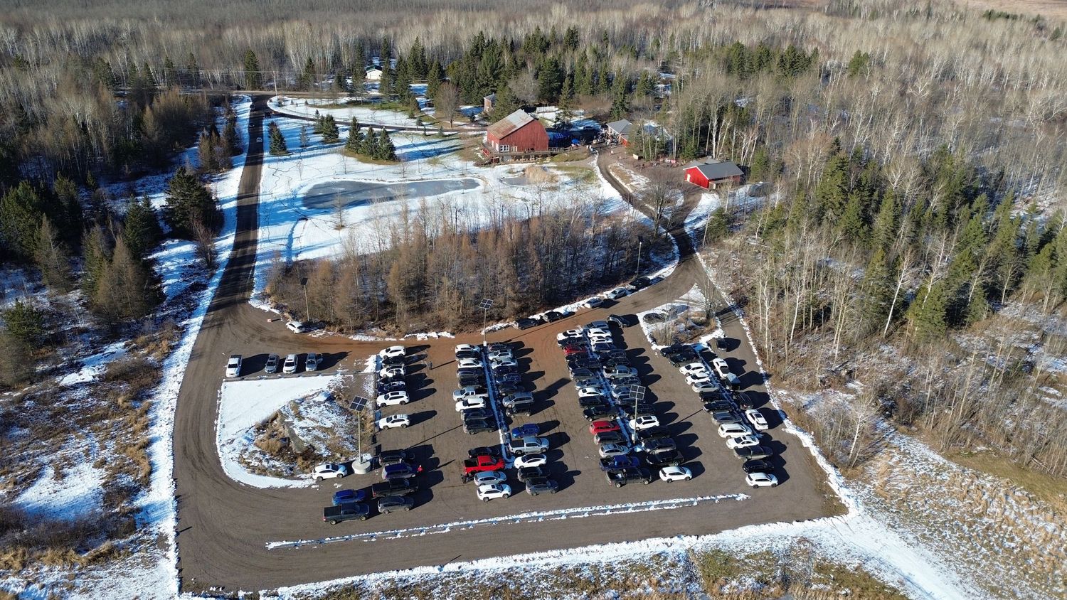 Aerial view of a winter venue with parking lot and buildings surrounded by snowy evergreen forest.