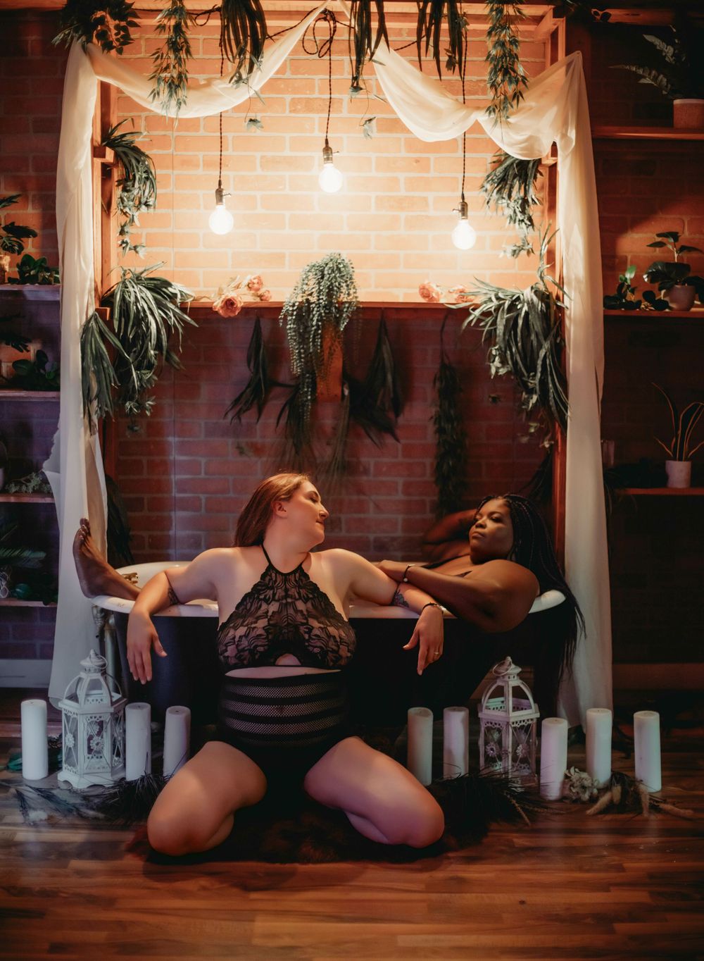 Romantic boudoir photo with draped fabric, hanging lights and plants against brick wall.