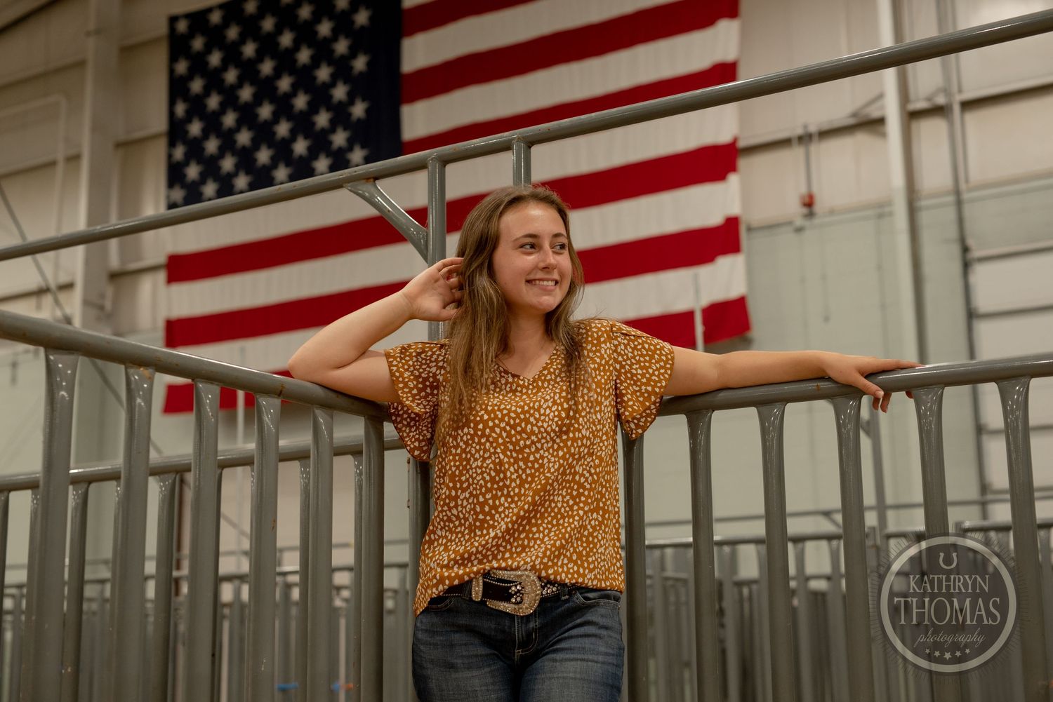 Energetic pose with arms spread against American flag in livestock facility.