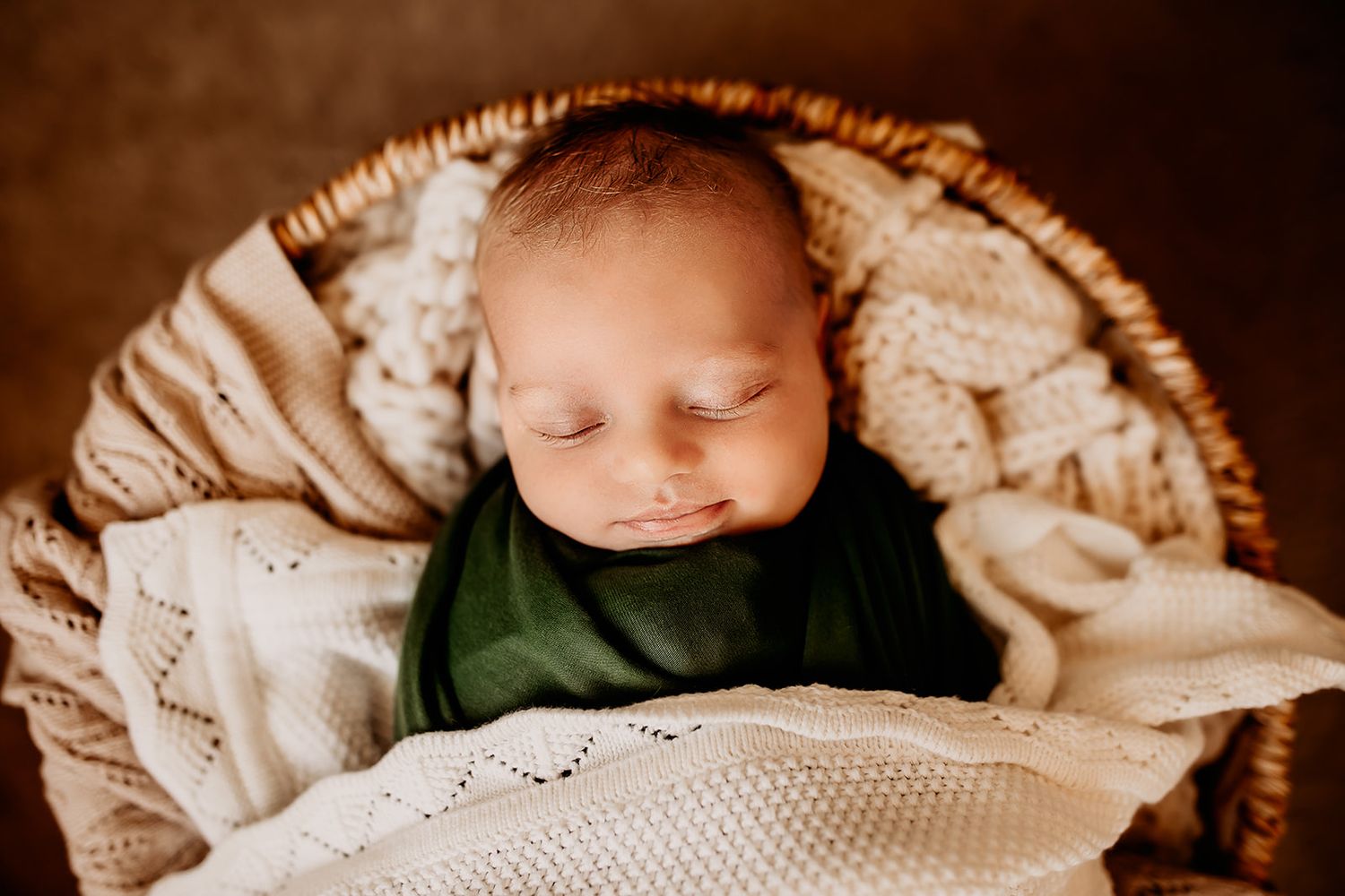 A newborn baby girl smiles while swaddled and laying in a basket for her newborn photos in Honolulu, Hawaii.