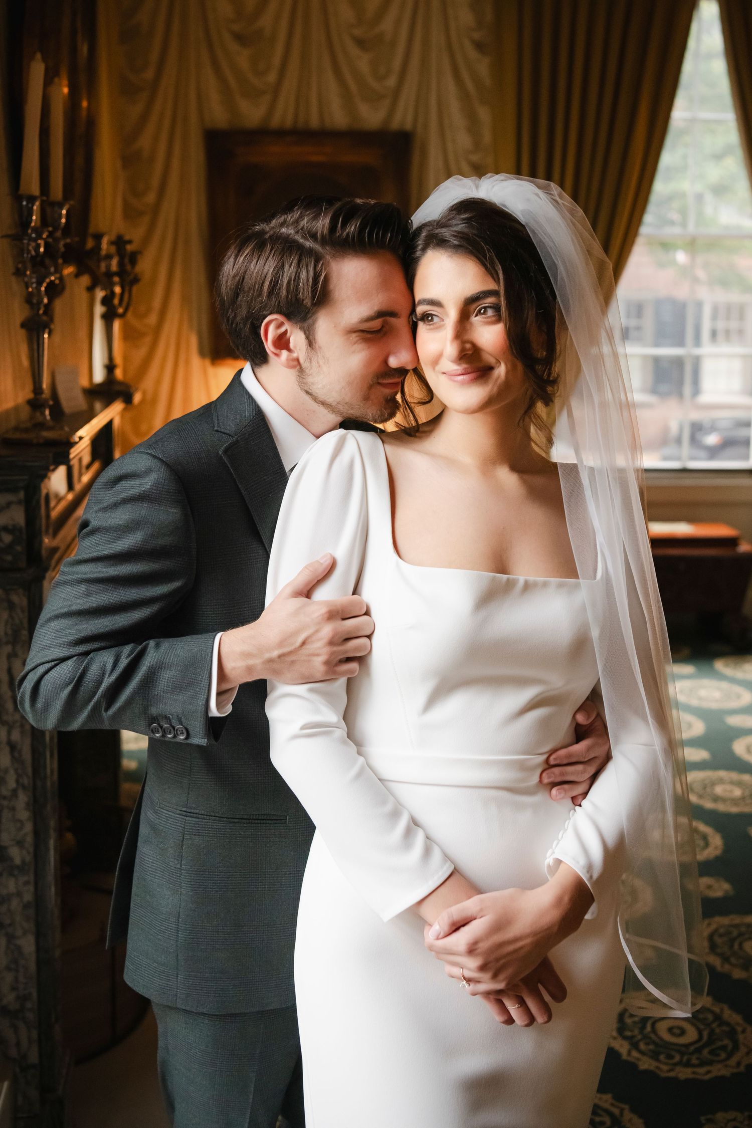 groom holds bride from behind in the soft window light of a historical Philadelphia venue