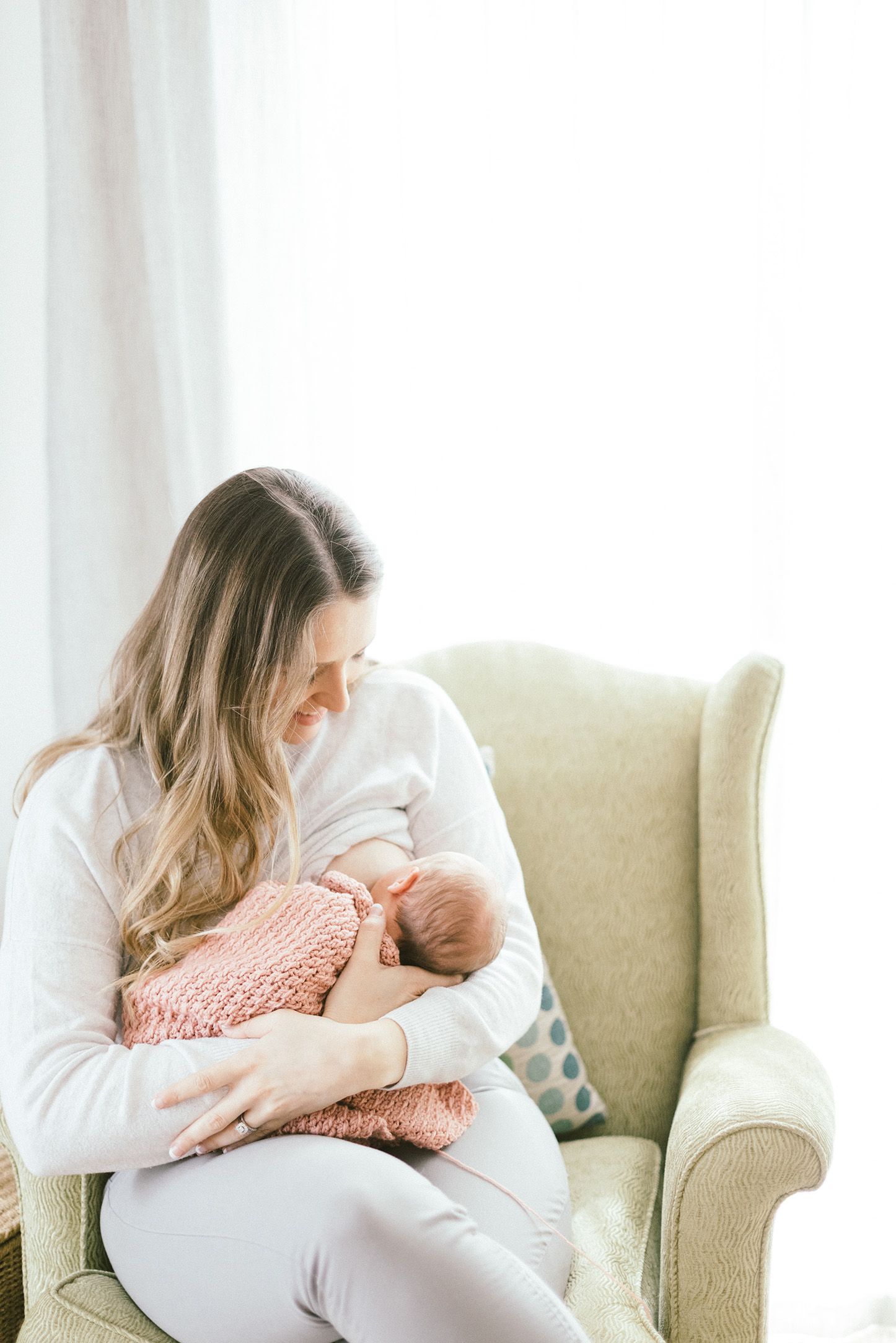 Nurturing moment in bright room as caregiver holds baby wrapped in pink blanket.