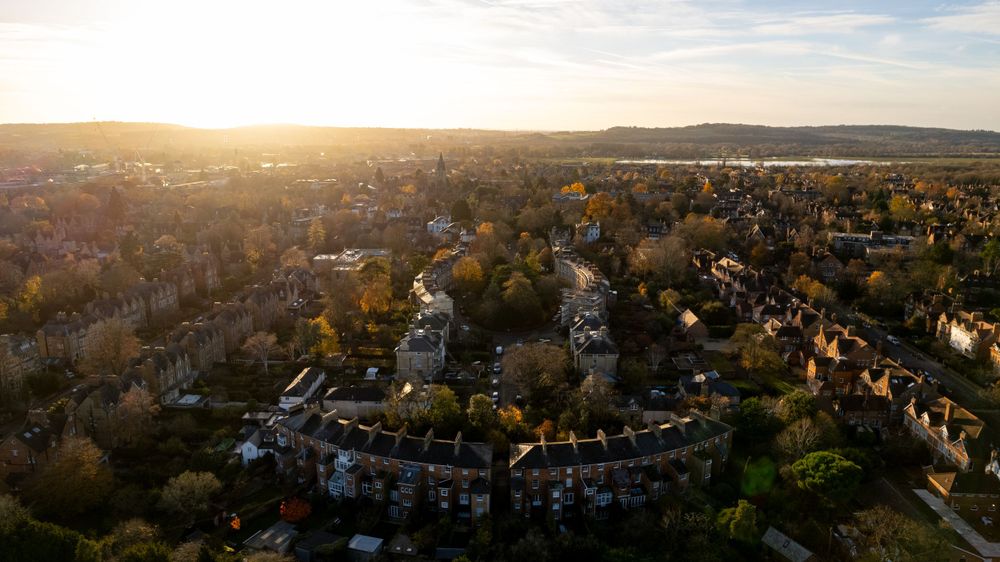 Aerial view of a residential neighbourhood with curved rows of houses, surrounded by trees, under a setting sun in the horizon.