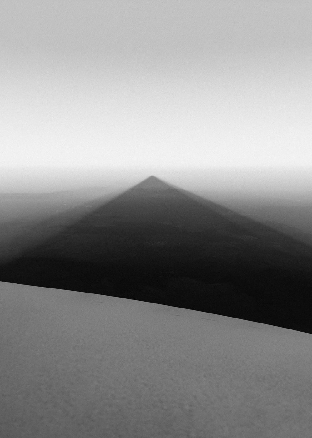 Dramatic black and white mountain shadow cast across snowy landscape at sunrise.