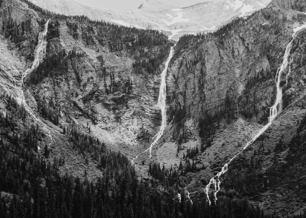 Black and white landscape of cascading waterfalls flowing down steep mountain cliffs.