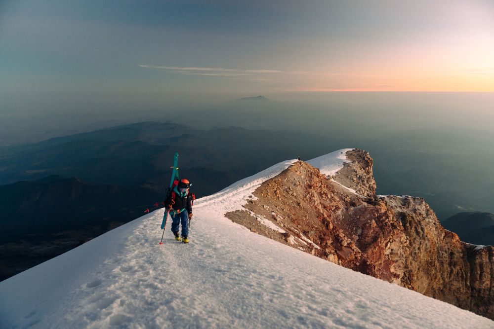 Winter mountaineers trek along snow-covered summit ridge at dawn.