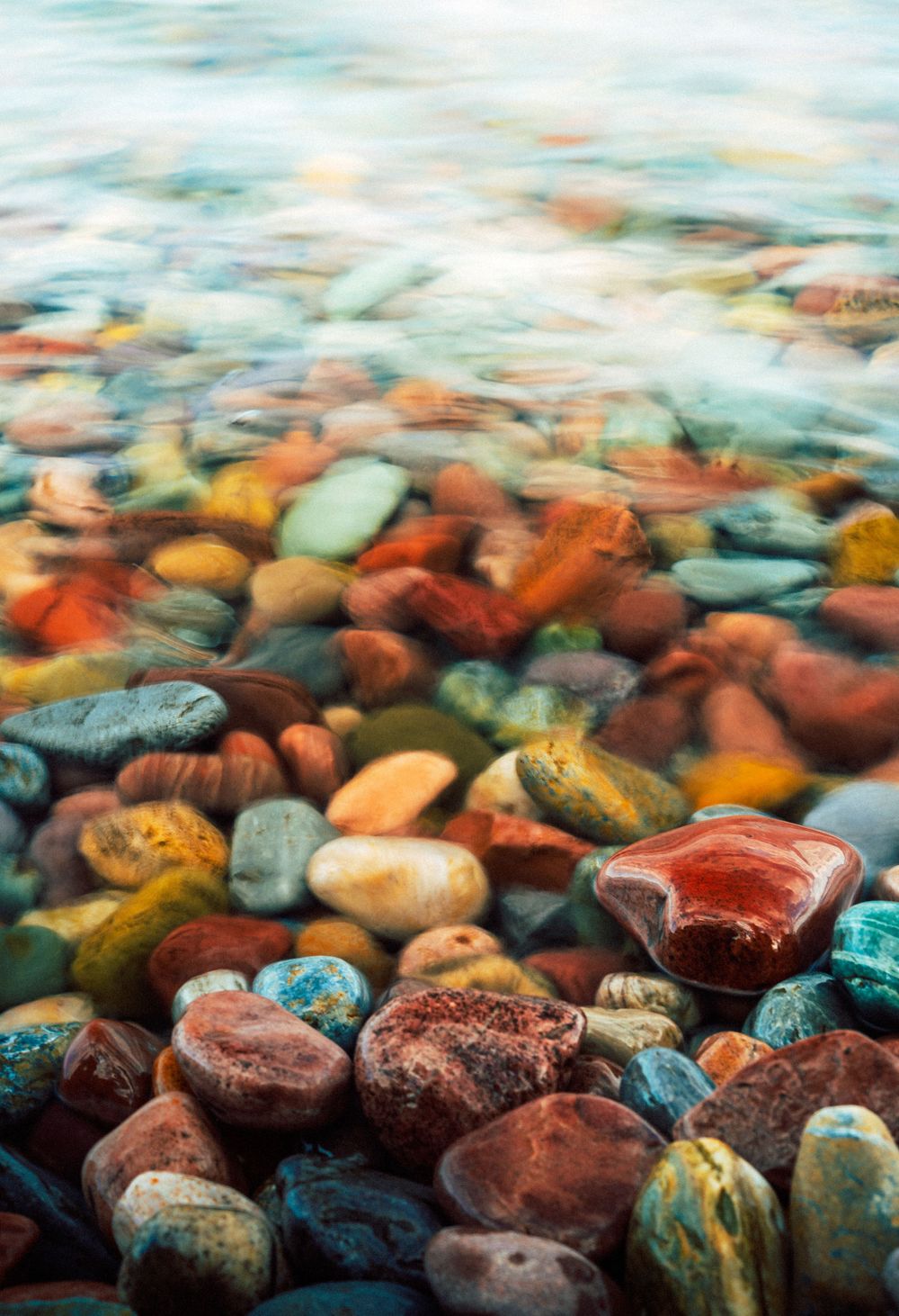 Colorful river rocks underwater create abstract patterns of red, blue and orange.