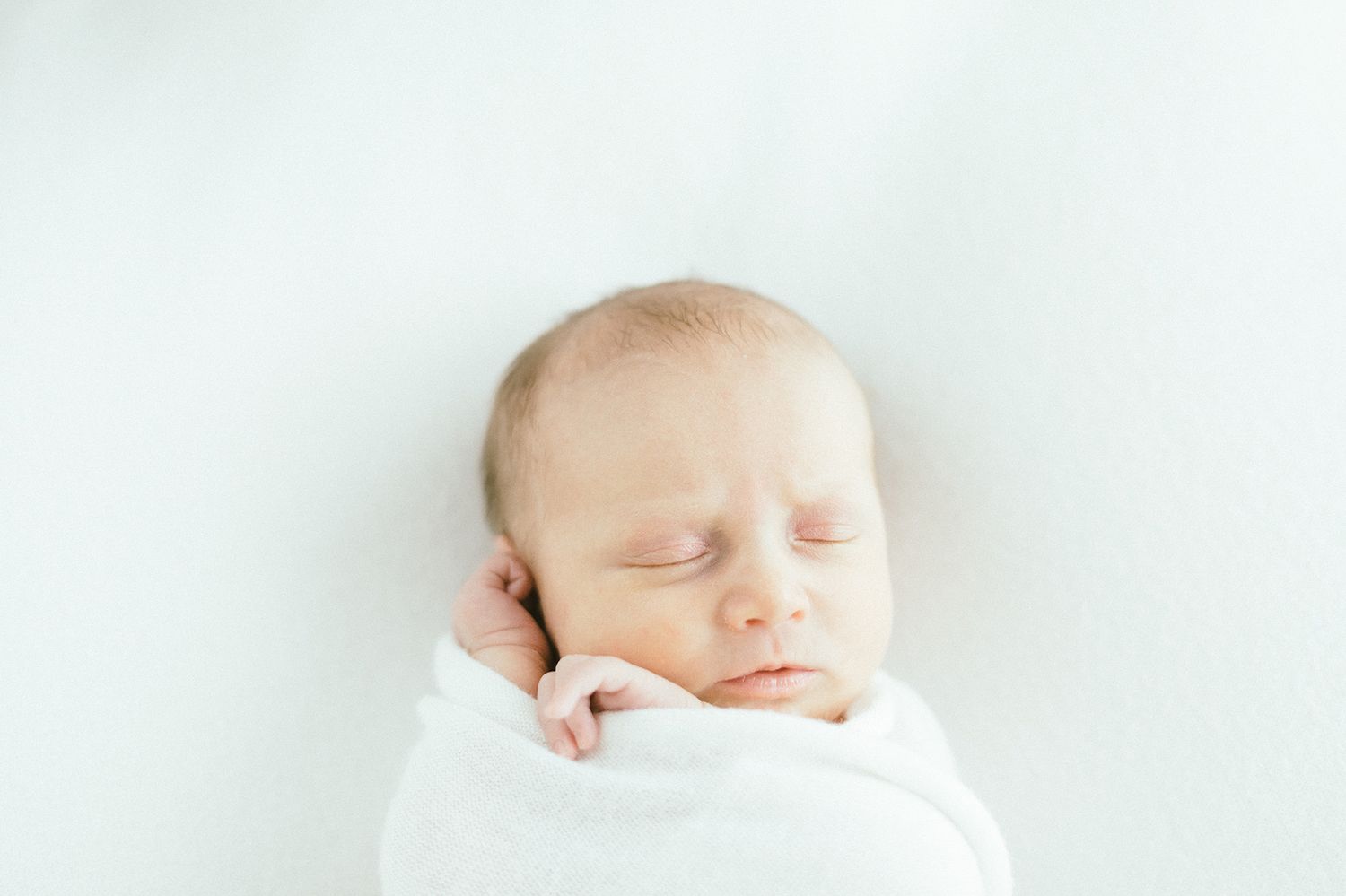 Serene newborn sleeping peacefully while swaddled in white.