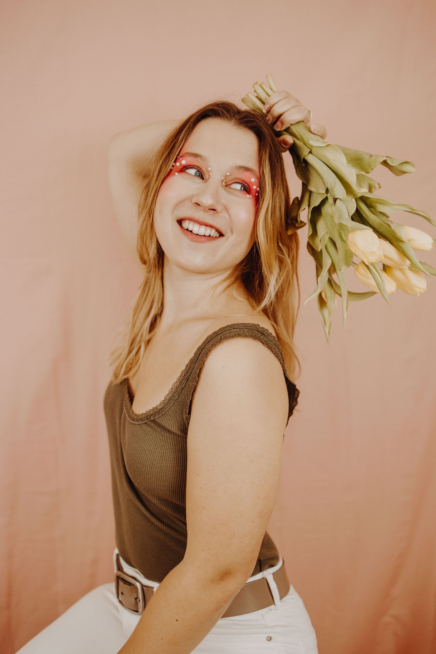 An artistic portrait with white tulips and warm peachy lighting against a neutral background.