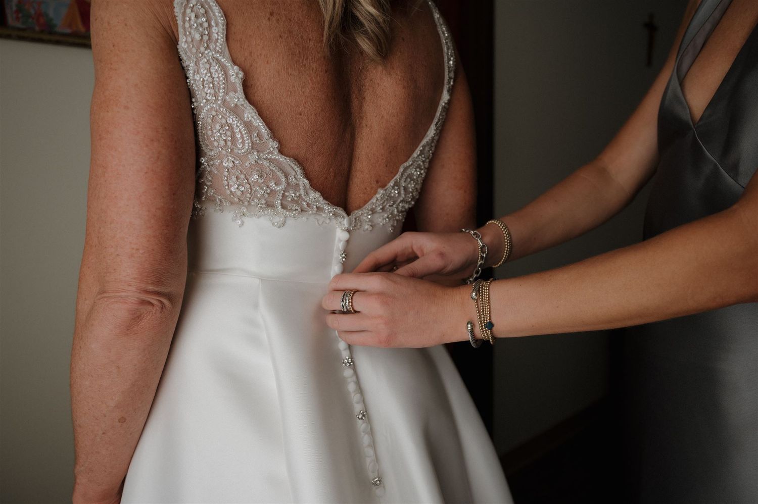 Close-up detail of buttons and lace on the back of a white wedding dress being fastened.