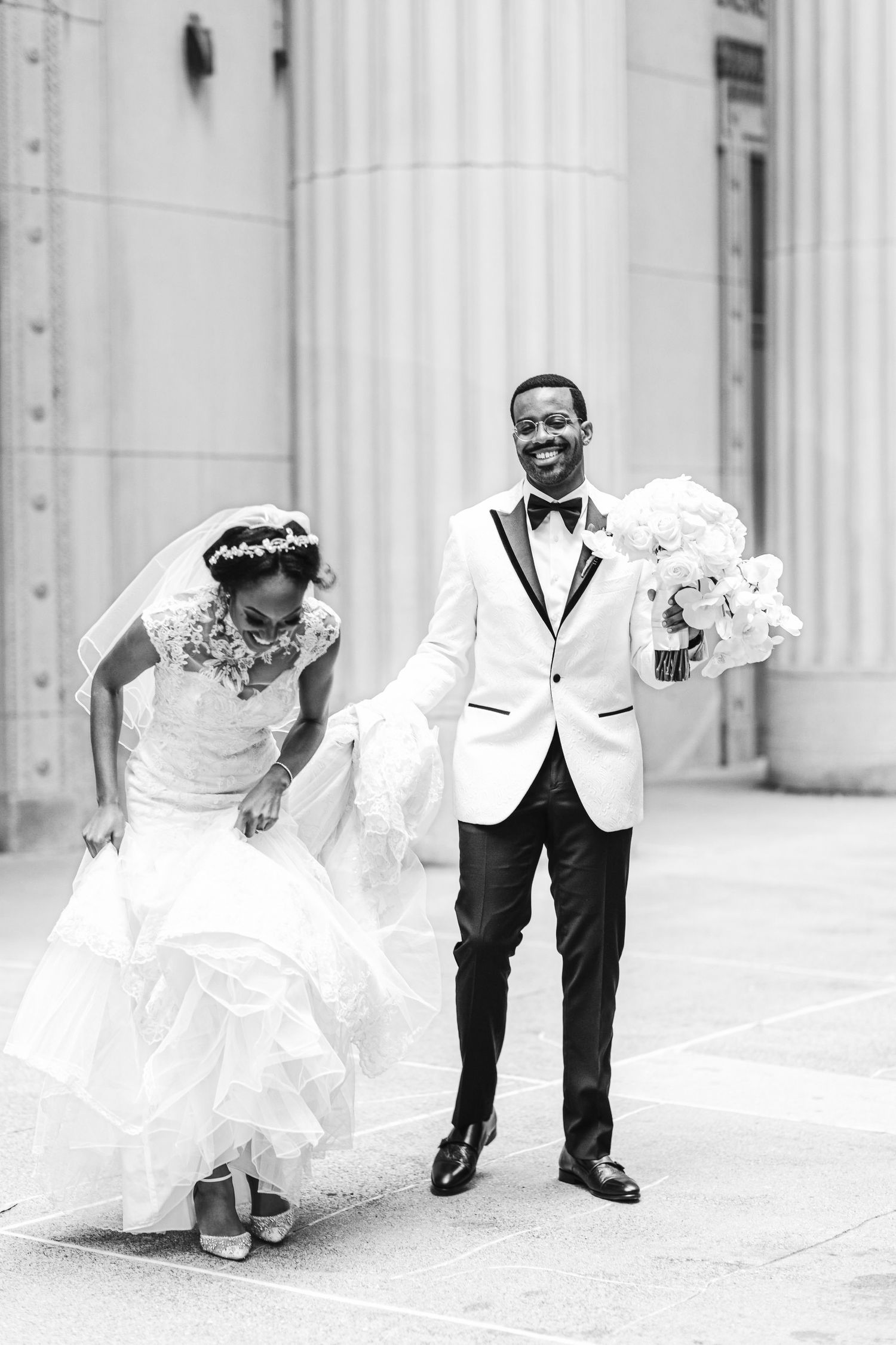 A playful wedding moment in black and white with classic architectural columns.