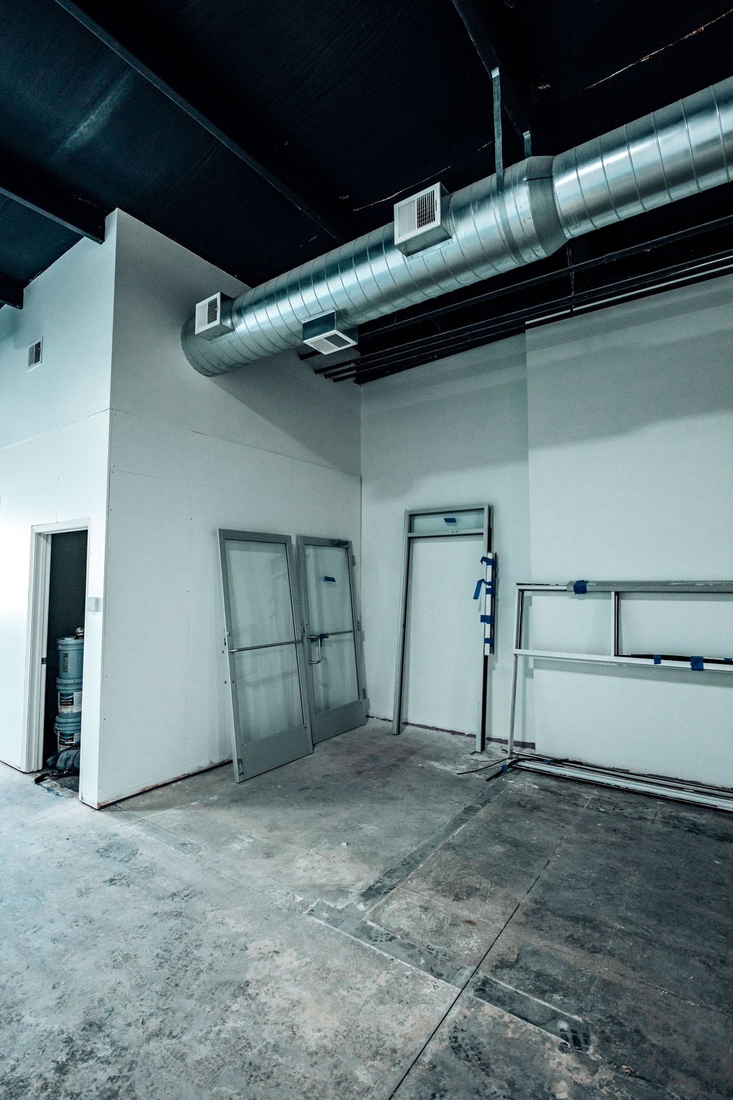 Industrial space with exposed ductwork and metal doors against white walls.