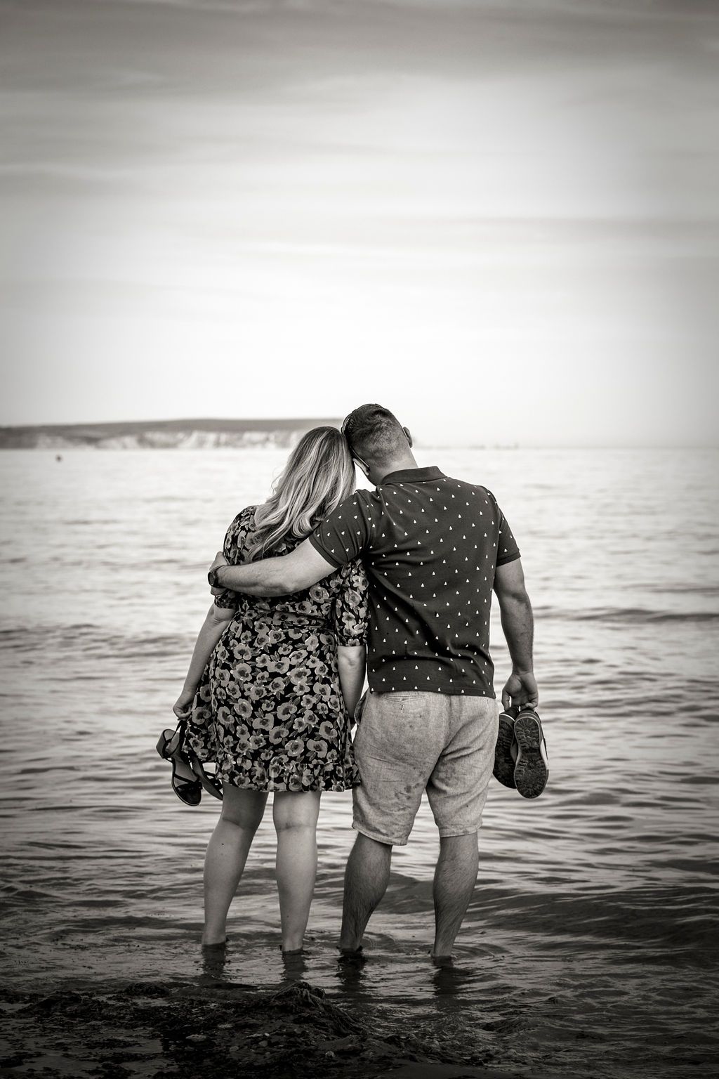 A black and white image of a couple standing in the ocean water looking at the horizon.
